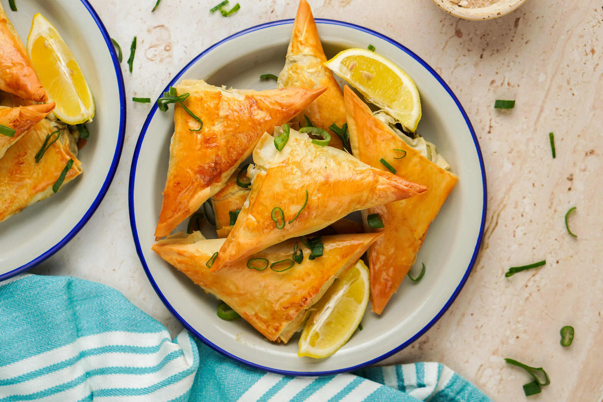 Spanakopita: fetasajtos-spenótos töltelékkel töltött réteslapbatyuk tányéron, citrommal és újhagymával tálalva