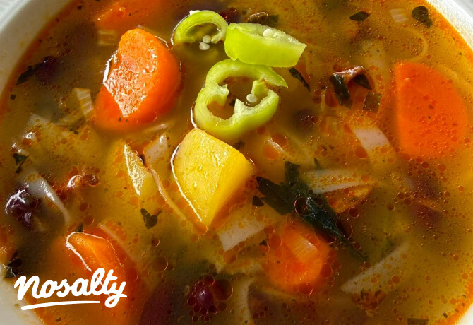 Tálban tálalt, aranysárga, zöldséges leves, amelyben sárgarépa-, burgonya- és hagymadarabok, valamint karikázott zöld paprika láthatók. A leves tetején apró zöldfűszerek és pirosas olajcseppek úsznak.