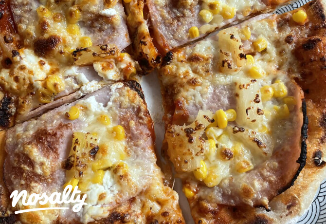 Frissen sült nápolyi pizza világos, levegős széllel, tetején olvadt sajttal, sonkaszeletekkel és aranysárga kukoricával. A pizzát négy szeletre vágták, a megpirult sajton és a hólyagos tésztaszélen jól látszanak a kemencében sült foltok.