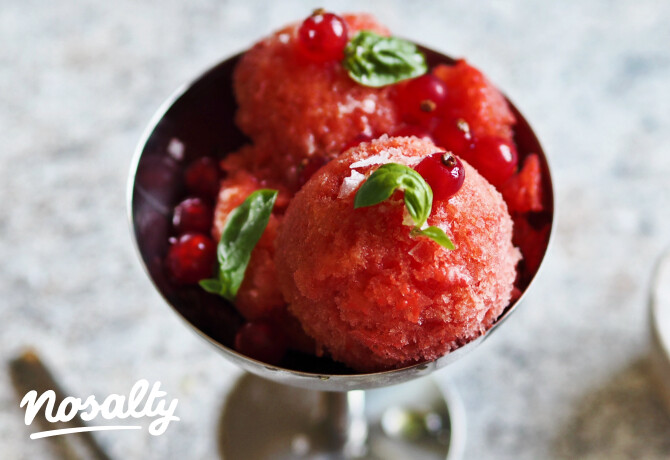 Házilag készített paradicsomsorbet fagyis kehelyben, ribizlivel és bazsalikommal díszítve