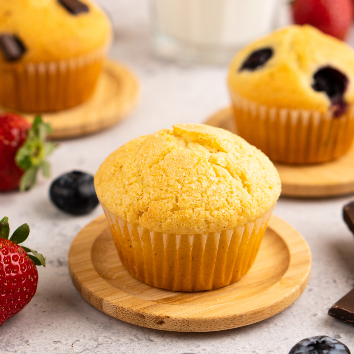 Natúr muffin kis fa alátéten, körülötte bogyós gyümölcsök, a háttérben további muffinok