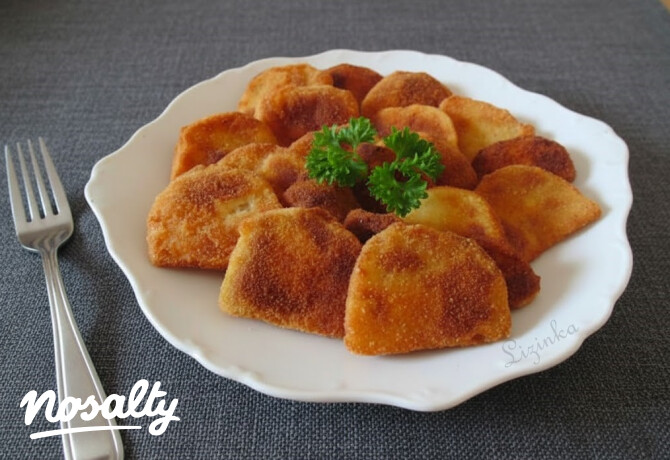 Frissen sült, aranybarna, panírozott karalábédarabok egy fehér tányéron, középen friss petrezselyemágakkal díszítve