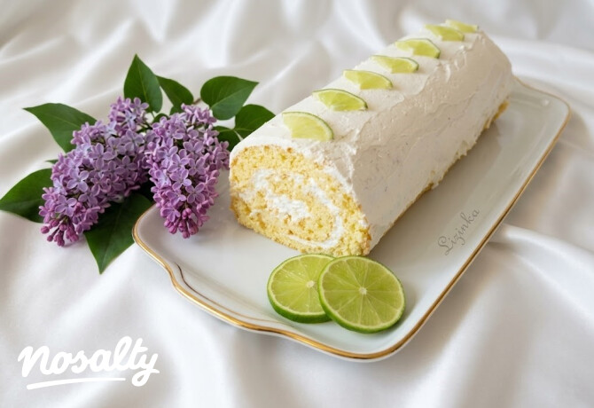 Limekarikákkal díszített, krémes lime-os rolád fehér tálcán, mellette friss lime és lila orgonavirág dekoráció.