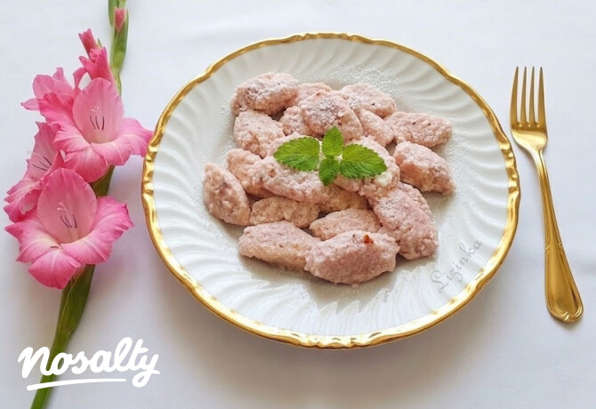 Rózsaszínes túrós galuskák aranyszegélyű fehér tányéron, mentalevéllel és pink virágokkal díszítve.