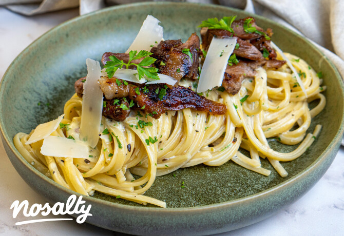 Krémes linguine pirult libahúsdarabokkal, vékony sajtszeletekkel és friss petrezselyemmel megszórva, zöld kerámiatányéron tálalva.